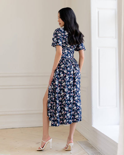 Woman wearing a navy floral dress standing in a room with a window.