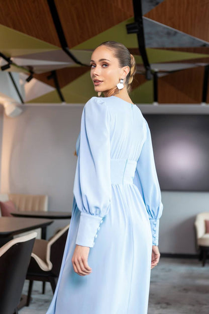 Woman in a light blue dress standing in an indoor setting with geometric ceiling design.