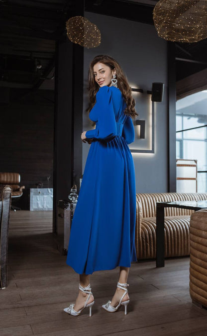 Woman in a blue dress standing in an elegant room with modern decor.