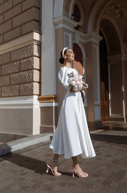 Woman in a white dress holding flowers in front of an architectural building