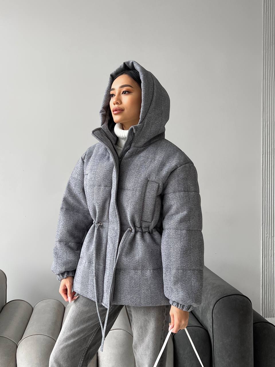 Person wearing a gray hooded jacket standing against a plain background