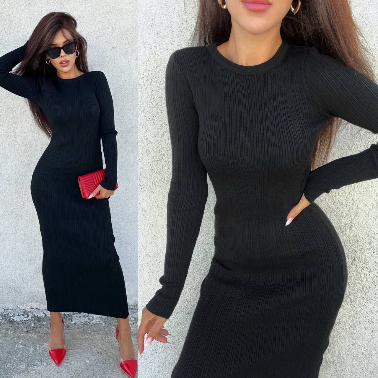 Woman wearing a black ribbed dress with long sleeves against a light gray wall.