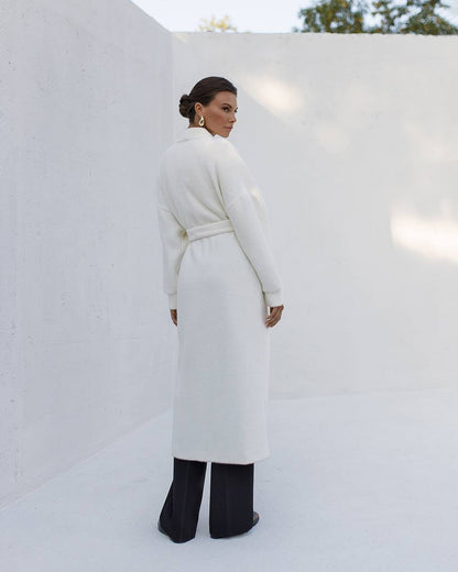 Woman wearing a long white coat against a white background