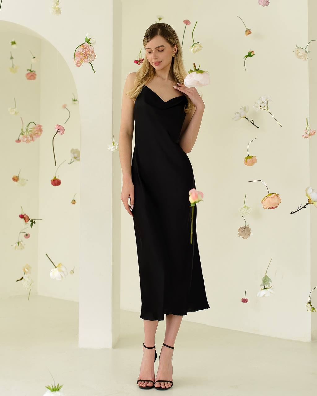 Woman in a black dress standing against a floral decorated wall.