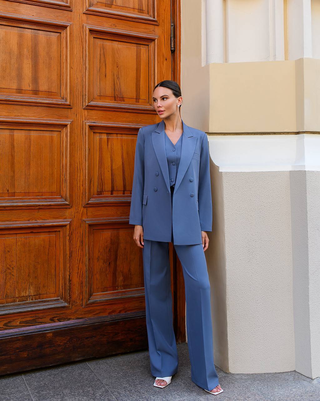 Woman in a blue suit standing in front of a wooden door.
