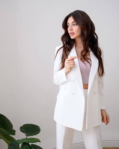 Woman wearing a white suit standing against a plain background
