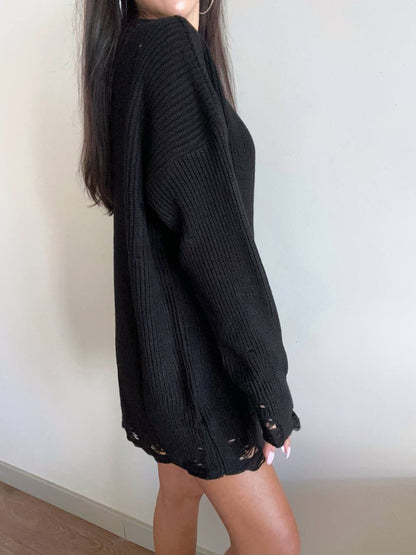 Person wearing a black ribbed sweater with distressed details on a plain background