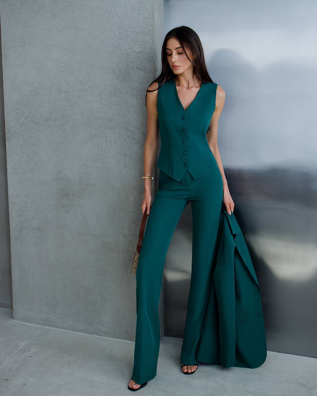 Woman in a teal jumpsuit standing against a gray wall.