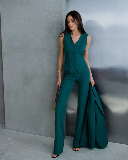 Woman in a teal jumpsuit standing against a gray wall.
