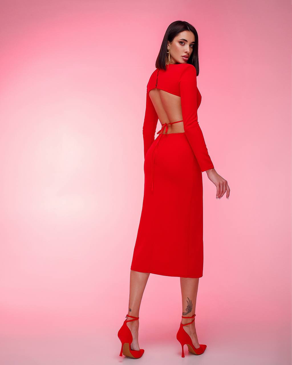 Woman wearing a red dress with cut-out design on a pink background