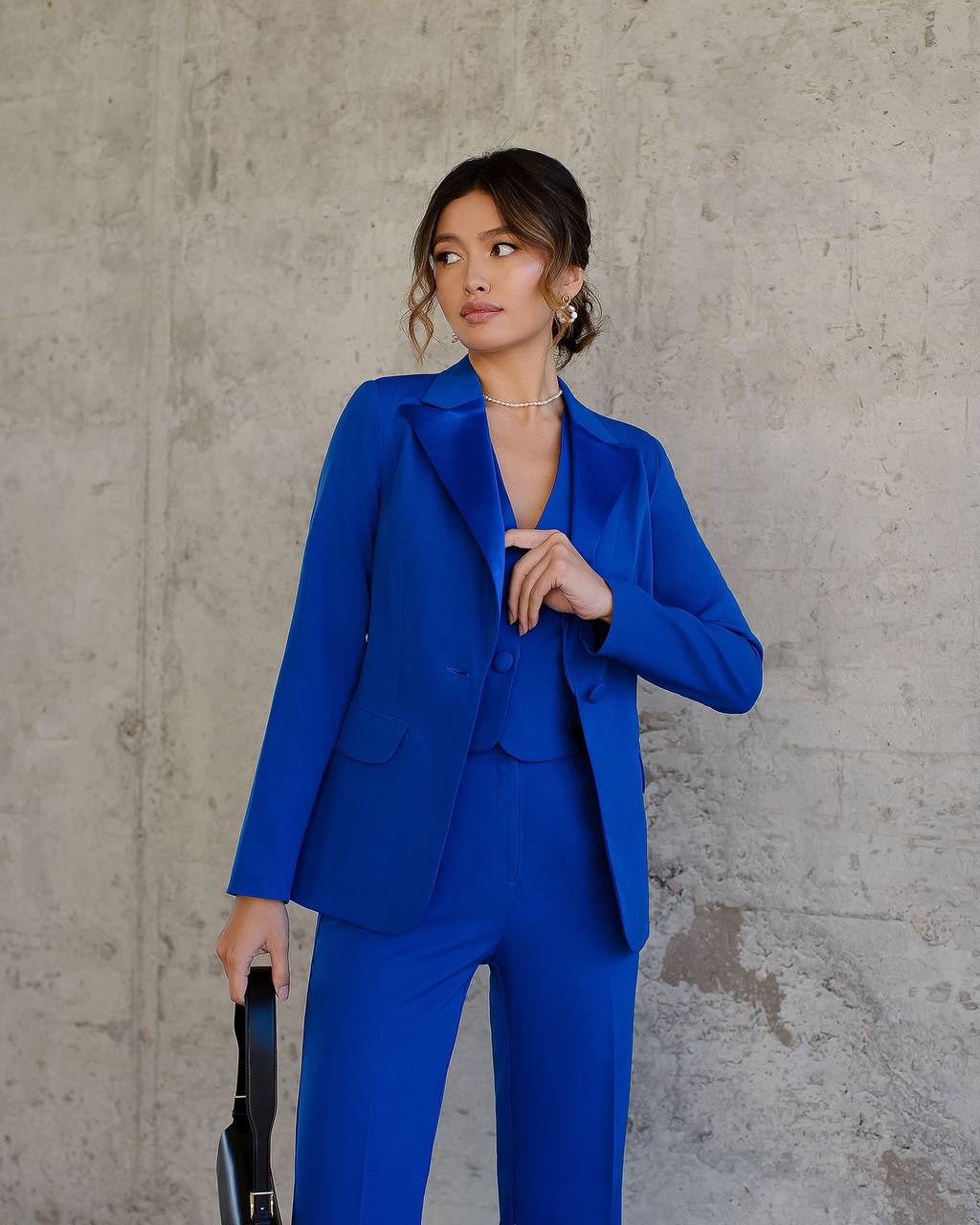 Woman wearing a blue suit standing against a concrete wall.