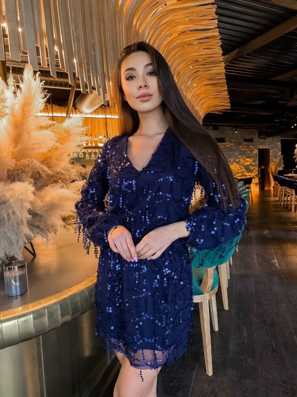 Woman in a blue sequin dress standing in a stylish interior setting.
