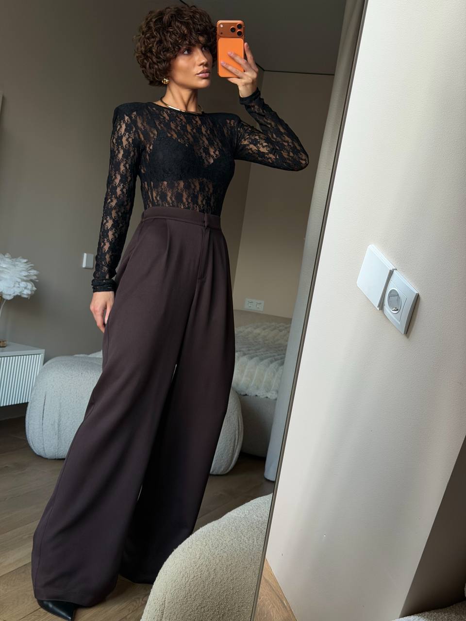 Woman taking a mirror selfie wearing a black lace top and brown wide-leg pants.