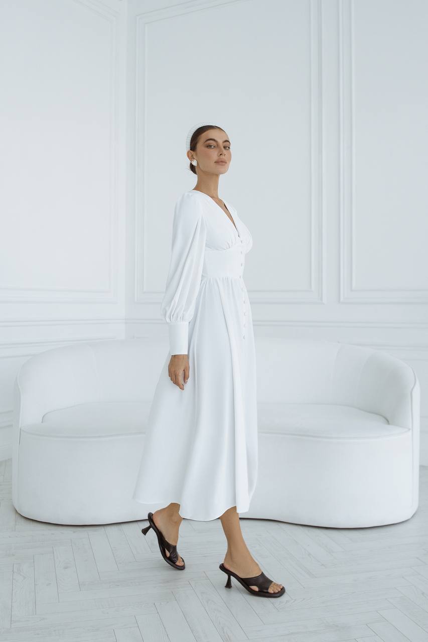 Woman in a white dress standing in a minimalistic room with a white couch.
