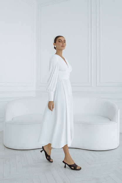 Woman in a white dress standing in a minimalistic room with a white couch.