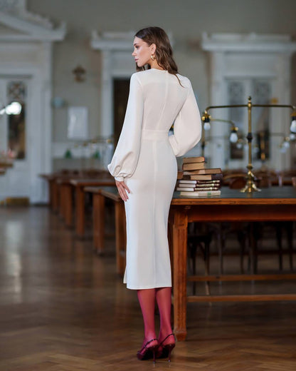 Woman in a white outfit standing in a room with wooden floors and furniture.