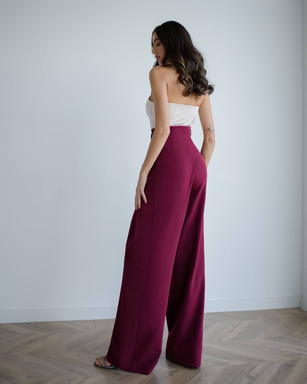 Woman wearing a white top and burgundy wide-leg pants against a plain background