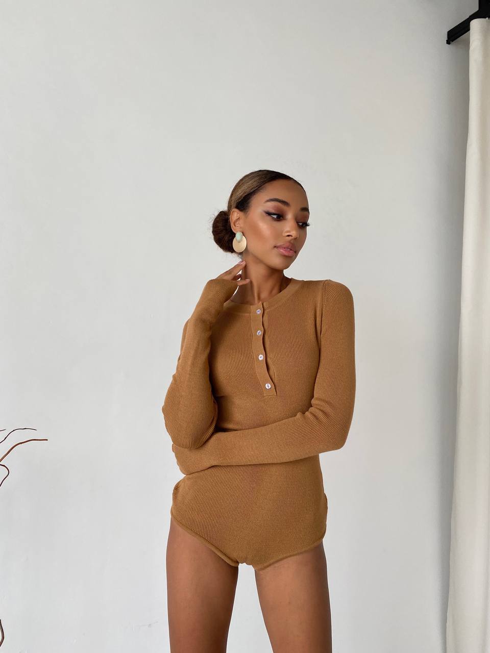 Woman wearing a brown long-sleeve top and high-waisted pants against a white background
