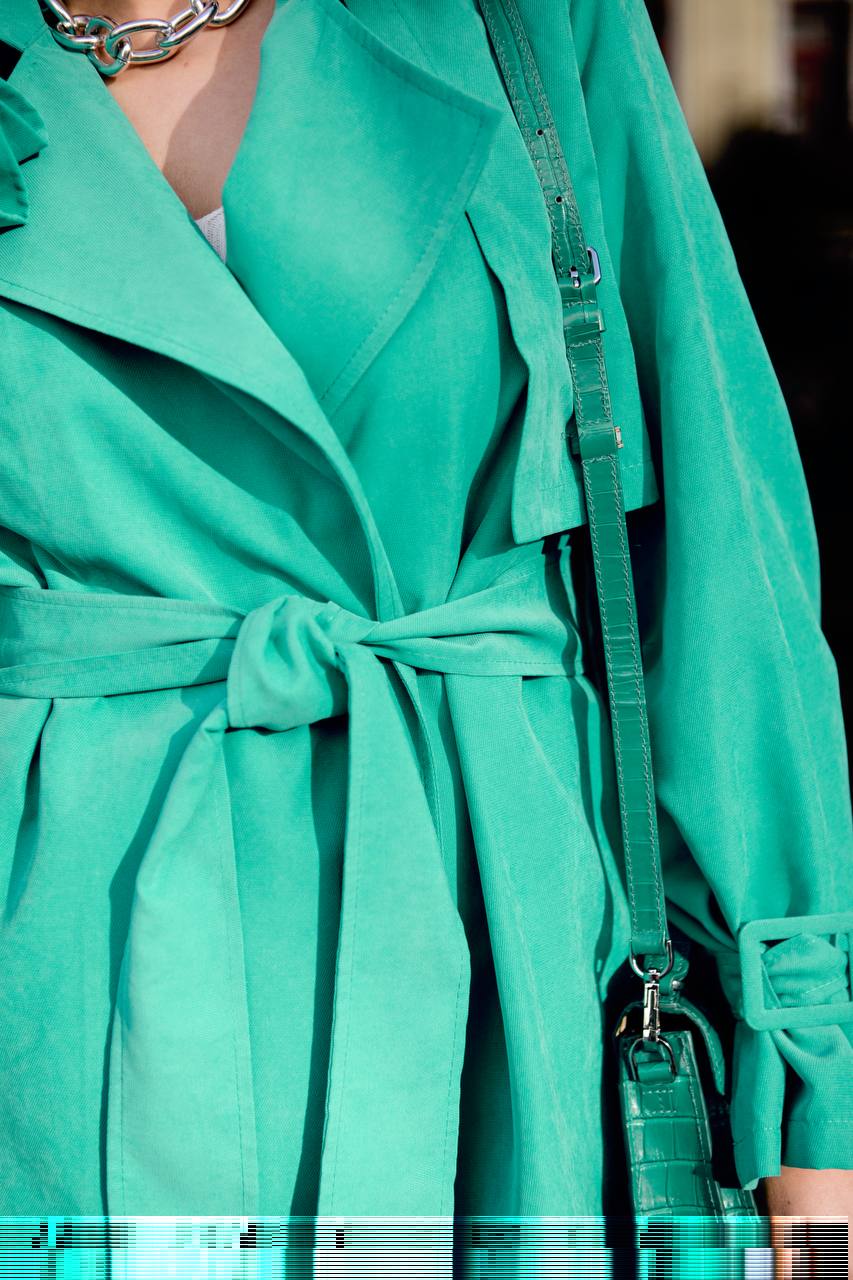 Close-up of a teal trench coat with a belt and handbag.
