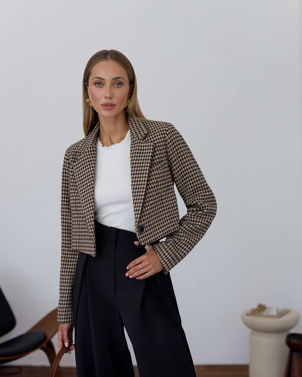 Woman wearing a checkered blazer over a white top and black pants against a plain background