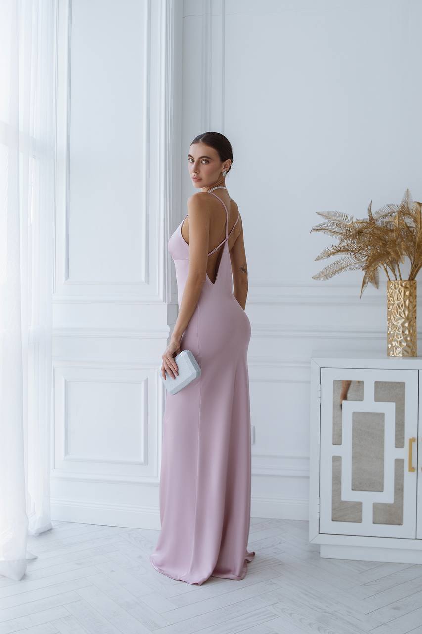 Woman in a pink evening gown standing in a stylish room with white walls and decorative elements.
