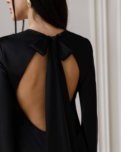 Black dress with open back and bow detail on a neutral background