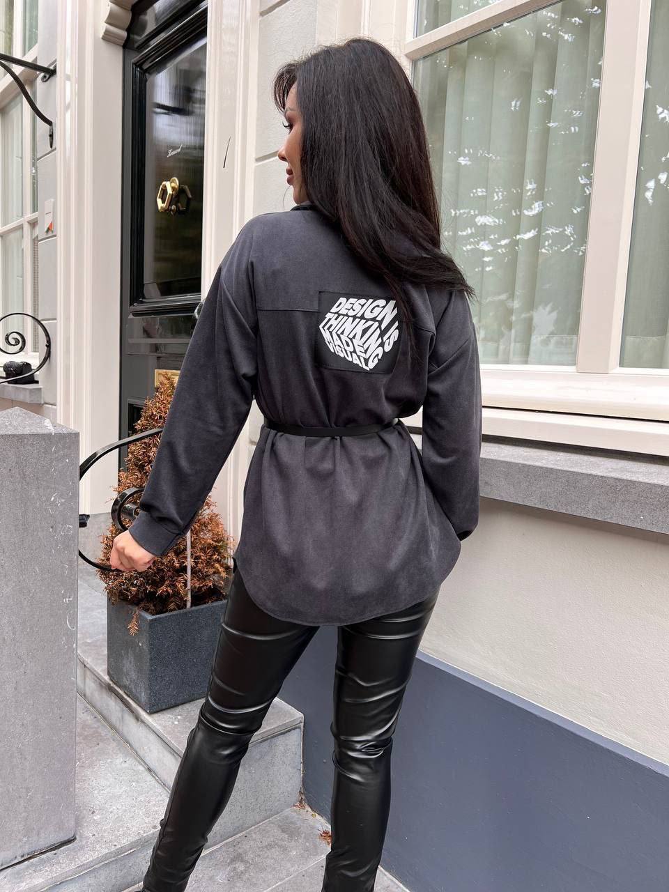 Person wearing a black jacket with a brand logo, standing outside a building.