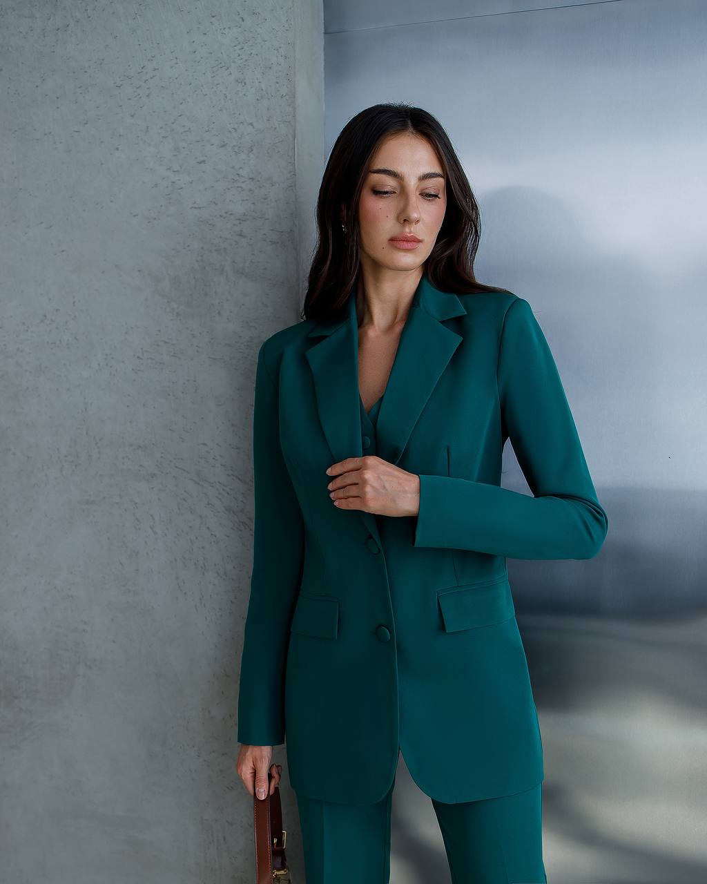 Woman in a teal suit standing against a gray wall.