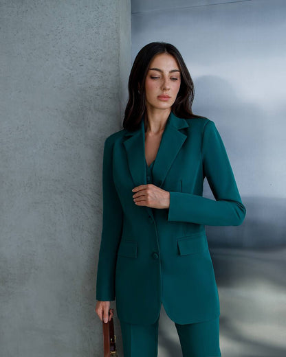 Woman in a teal suit standing against a gray wall.