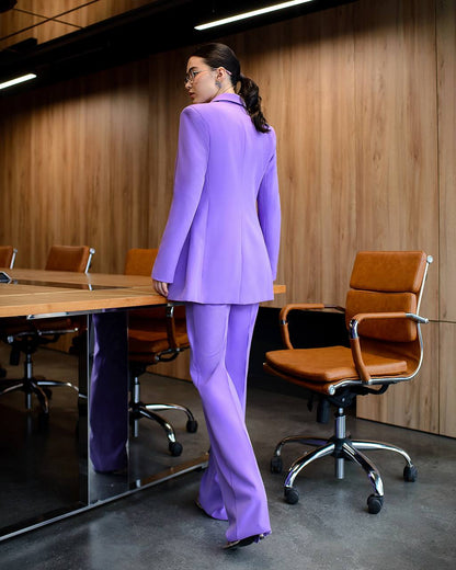 Person wearing a purple suit standing in an office setting with wooden walls and brown chairs.