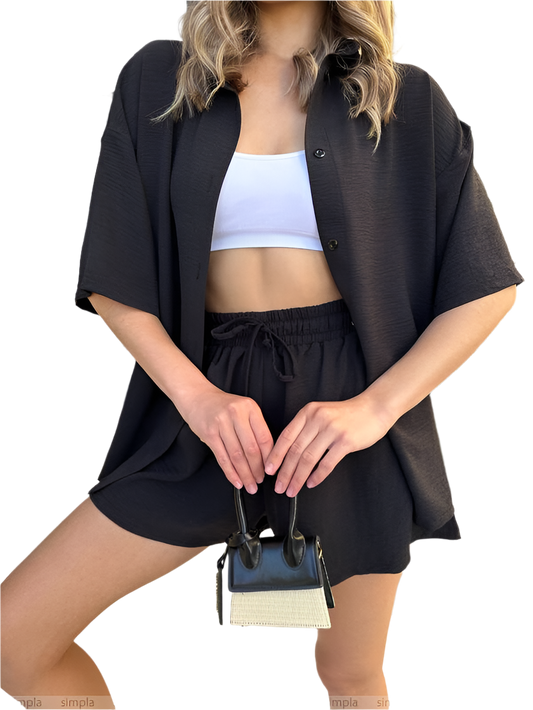 Person wearing a black outfit with a white top and holding a small handbag on a plain background