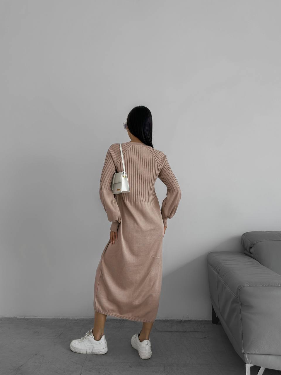 Woman in a beige ribbed dress standing in a minimalistic room with a gray sofa.