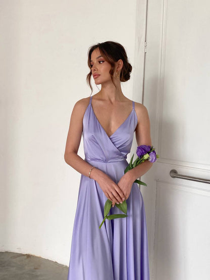 Woman in a lavender dress holding flowers against a white door.