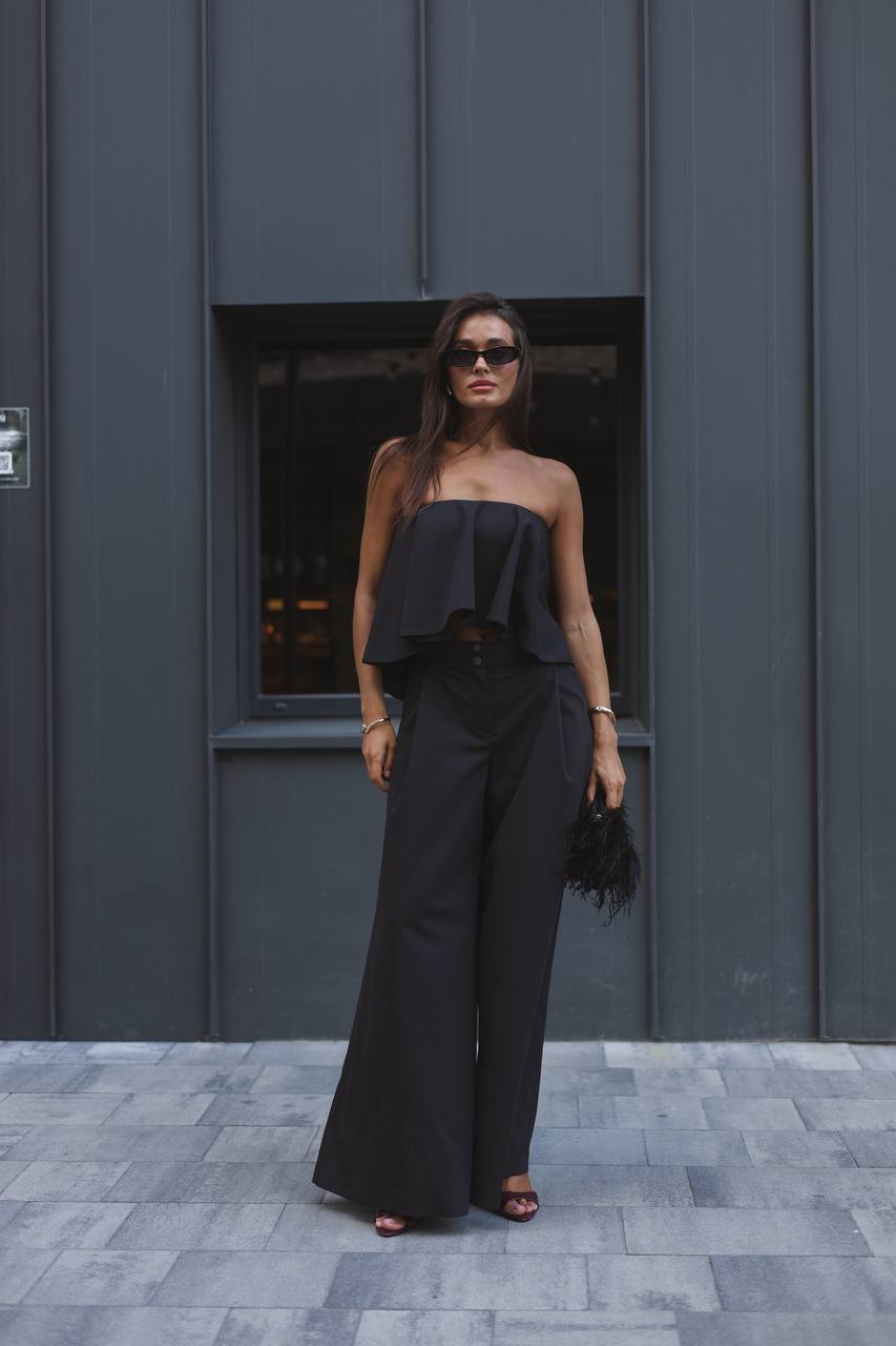 Woman wearing a black outfit standing in front of a gray wall.