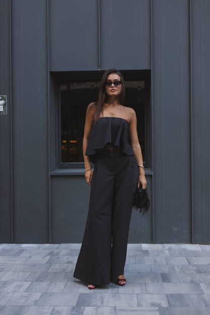 Woman wearing a black outfit standing in front of a gray wall.