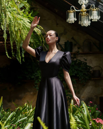 Woman in a black dress standing among plants with a chandelier in the background