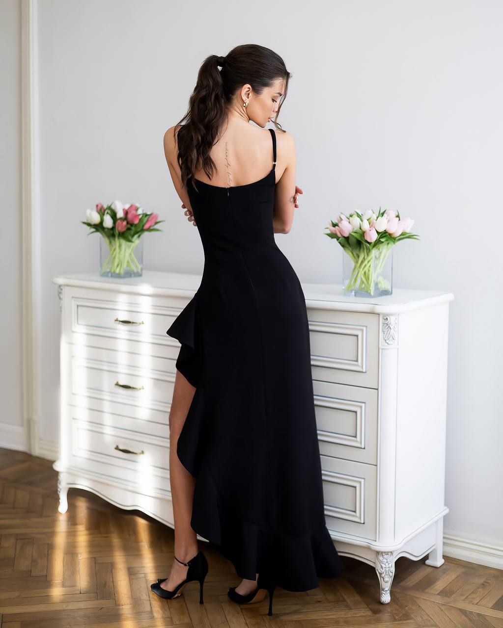 Woman in a black dress standing in front of a white dresser with floral arrangements.