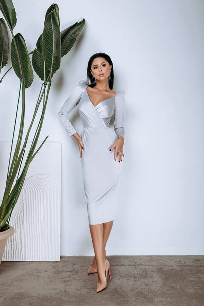 Woman in a white dress standing next to a large plant against a white wall.