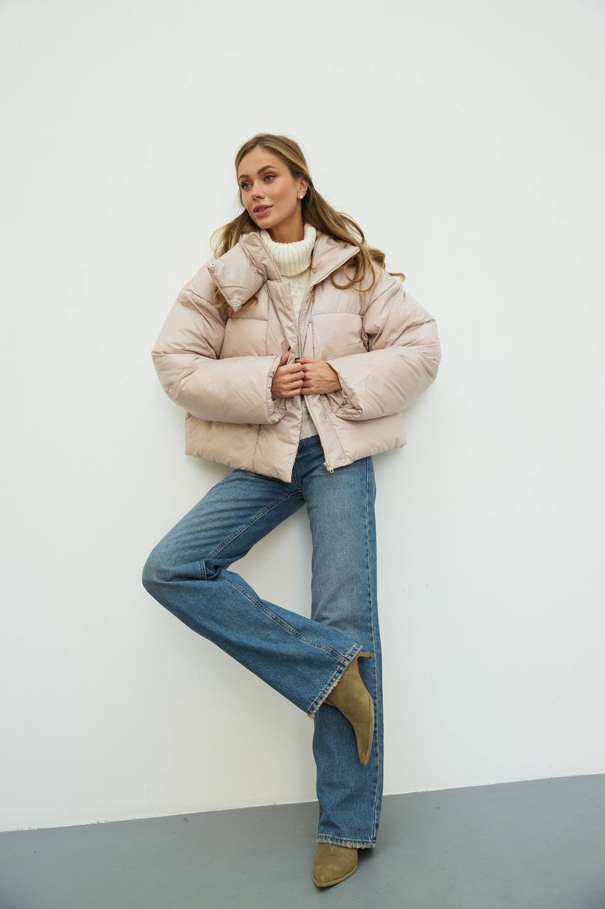Woman wearing a beige puffer jacket and blue jeans against a white background