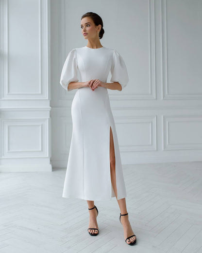 Woman wearing a white dress with puffed sleeves in a minimalistic room.