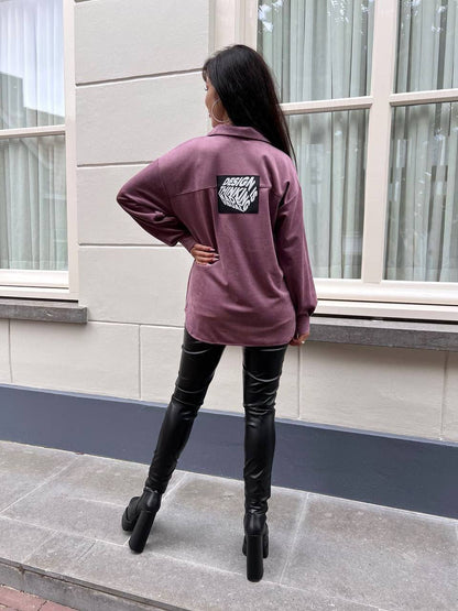 Person wearing a maroon sweatshirt with a logo on the back, standing outdoors.