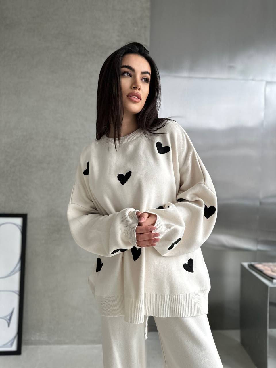 Woman wearing a white sweater with black heart patterns in a modern interior setting
