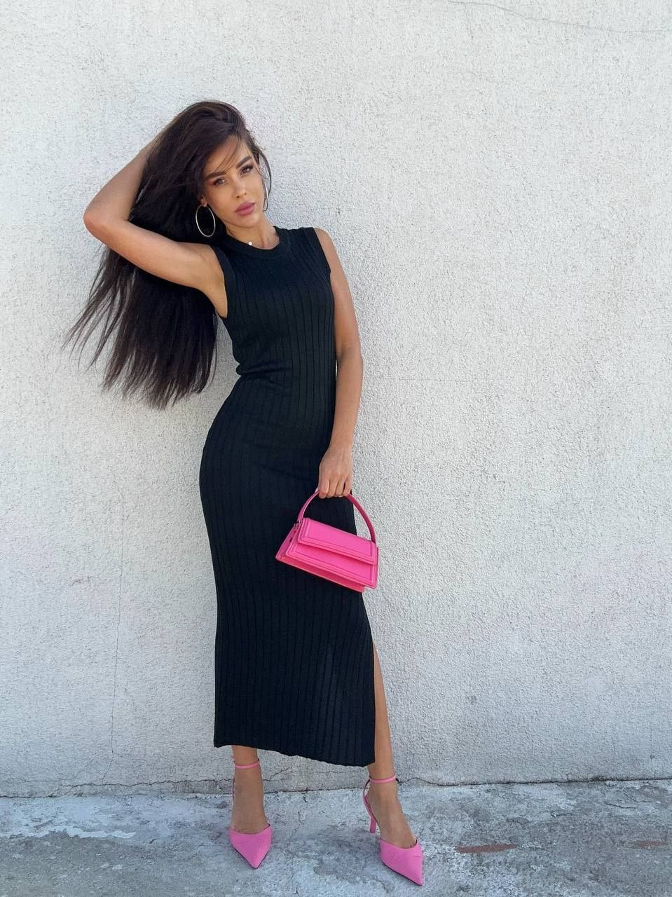 Woman in a black dress holding a pink handbag against a light gray wall.