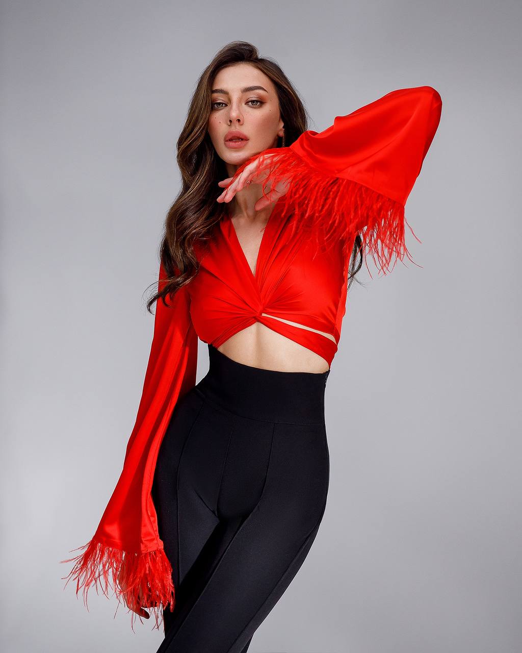 Woman wearing a red fringed top and black pants on a gray background