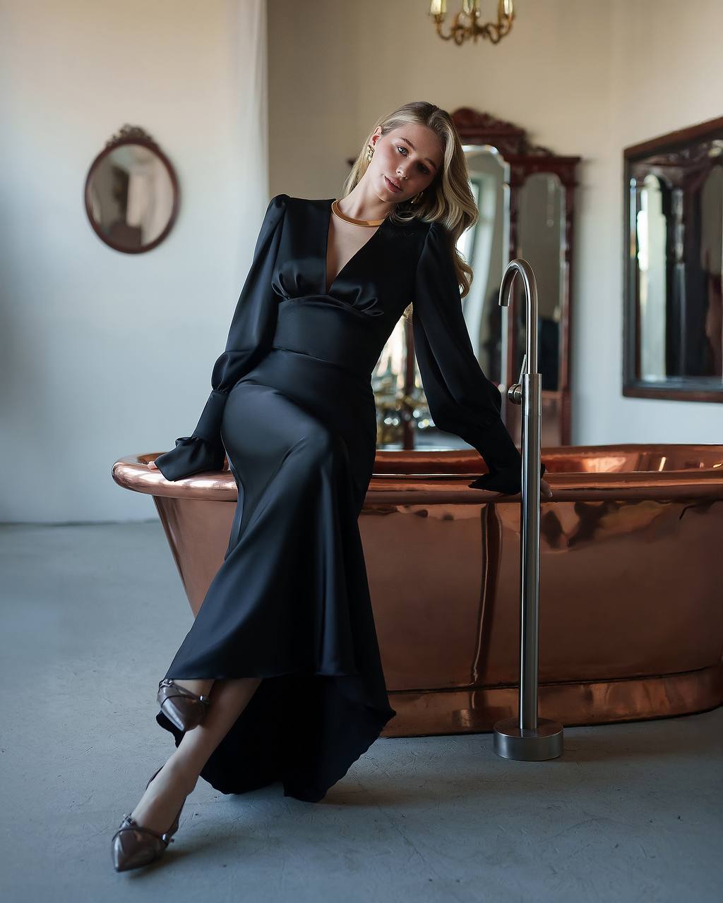 Woman in a black dress sitting on a copper bathtub in an elegant room.