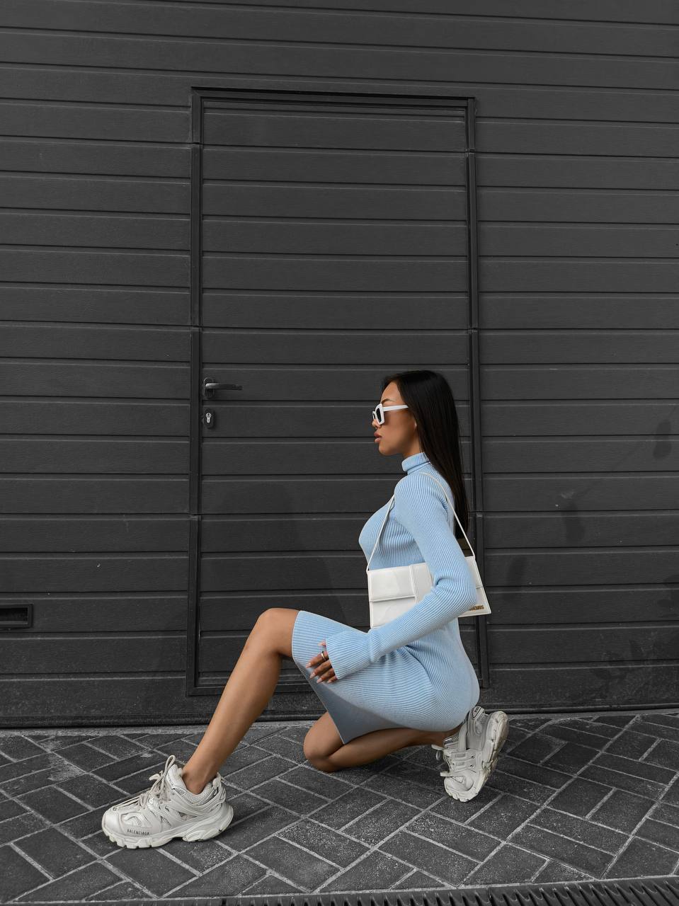 Woman in a light blue outfit posing in front of a black door.