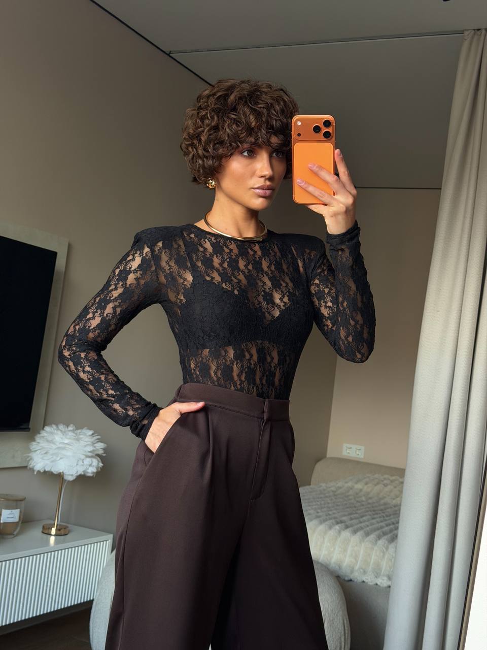 Person wearing a black lace top and brown pants taking a mirror selfie.