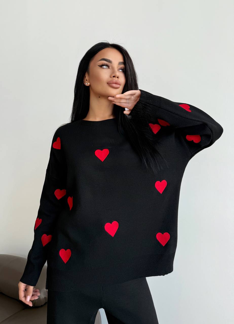Woman wearing a black sweater with red heart patterns against a plain background