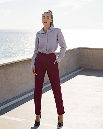 Woman in a light gray shirt and burgundy pants standing on a rooftop with water in the background