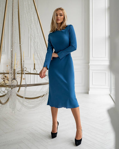 Woman in a blue dress standing in a stylish room with a chandelier.